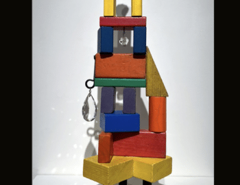 Abstract sculpture made from colored building blocks, wood thread spools, steel, crystal drawer pull, chandelier crystals, and black feet. Titled "Spolia #6" by Timothy DeVenney.